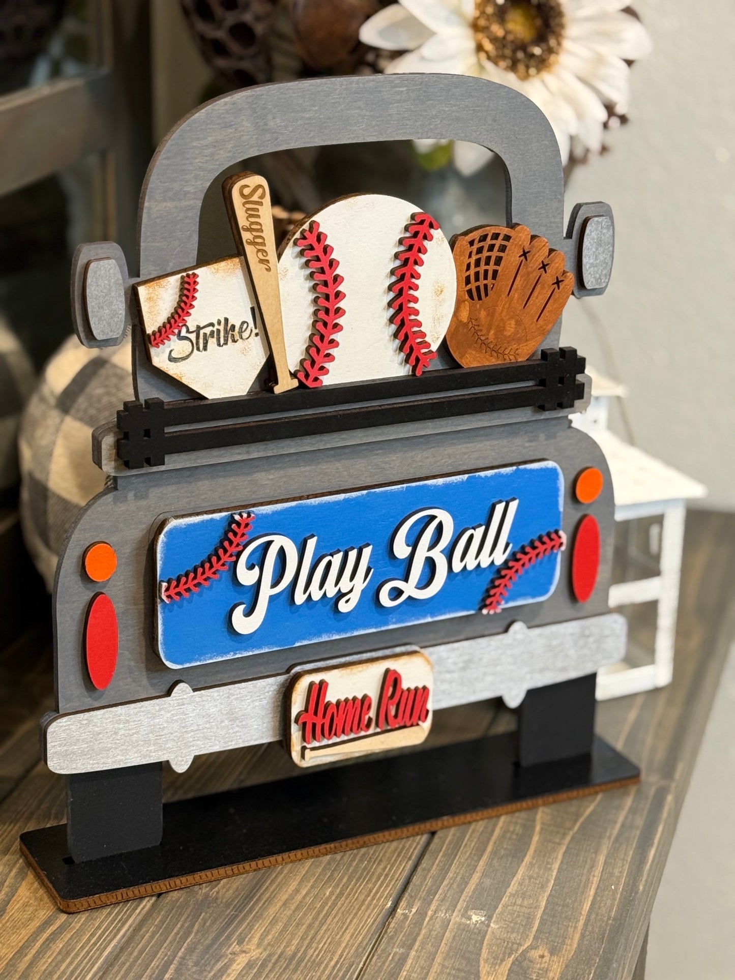 Side angle view of our farmhouse wooden truck shelf sitter filled with a baseball, a "Slugger" bat, and a glove, featuring a blue "Play Ball" tailgate and "Home Run" license plate interchangeable insert.